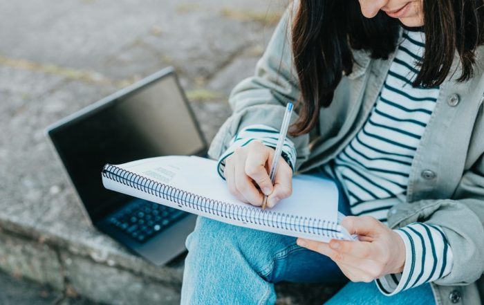 : A woman writing on a notepad with a laptop, for “Upcoming Courses at Kyra – What’s new