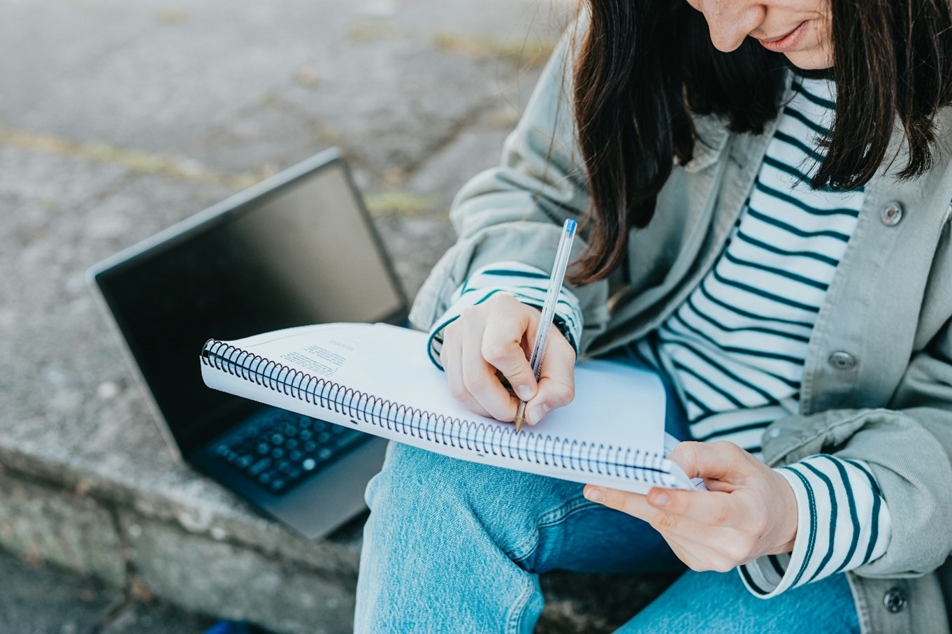 : A woman writing on a notepad with a laptop, for “Upcoming Courses at Kyra – What’s new